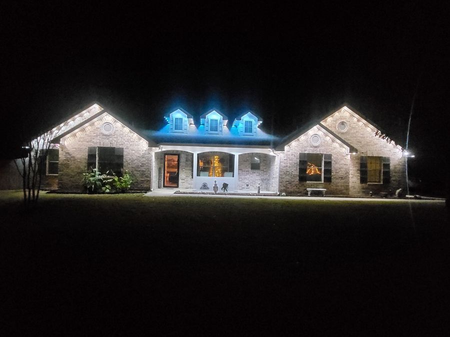Brick home with blue dormer lighting and warm white roofline