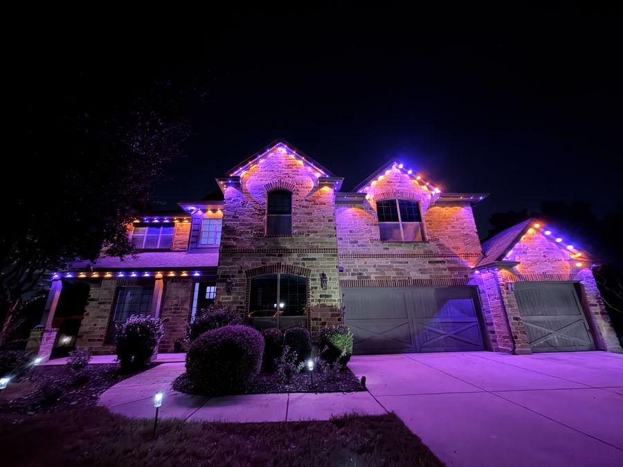 Two-story stone home in purple and orange permanent lighting